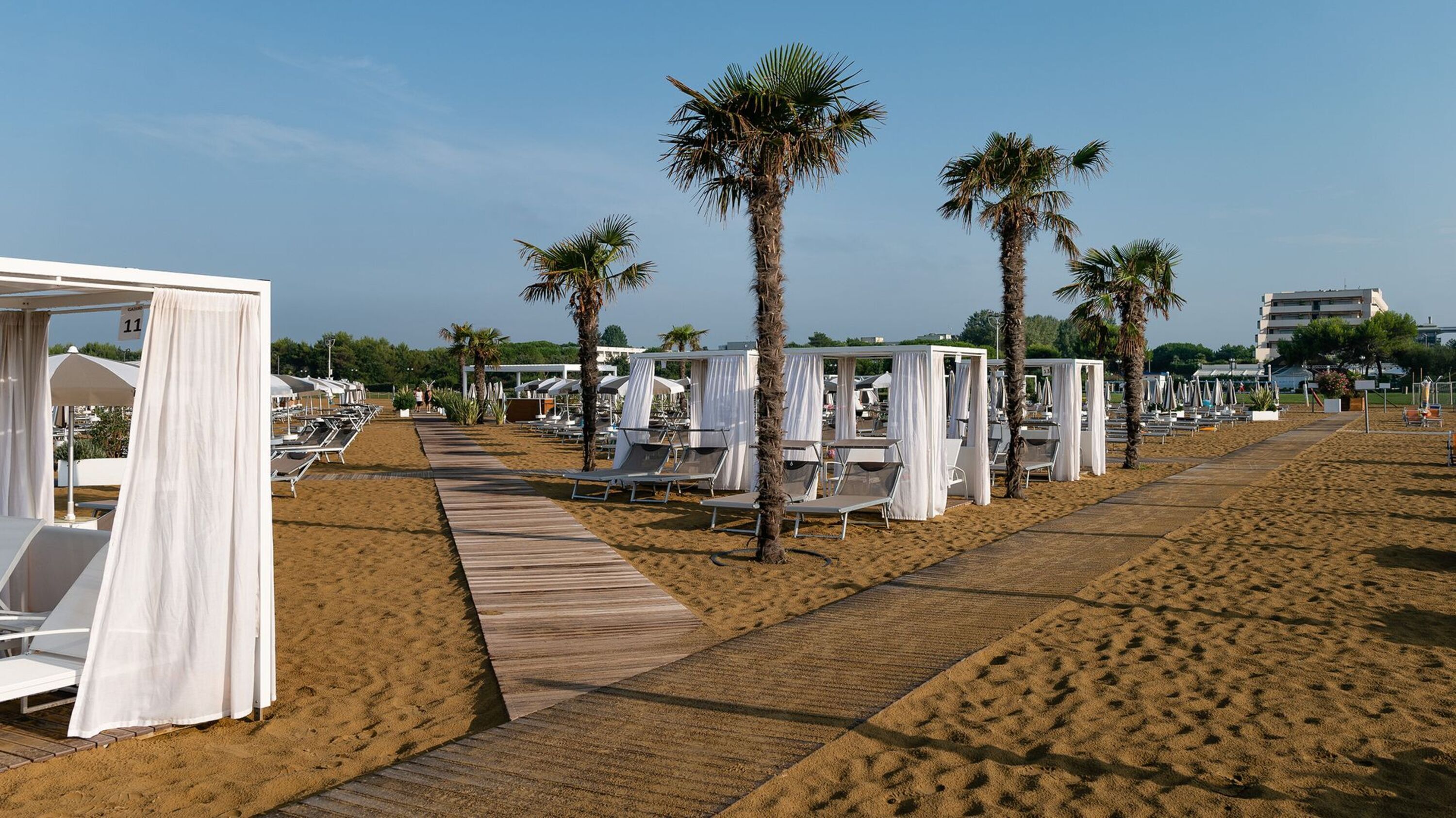 Un hôtel situé en bord de mer, doté de chaises longues, de palmiers et d’une promenade en bois.
