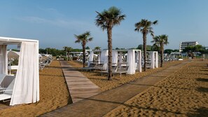 Un hotel al costat de la platja amb gandules, palmeres i un camí de fusta.
