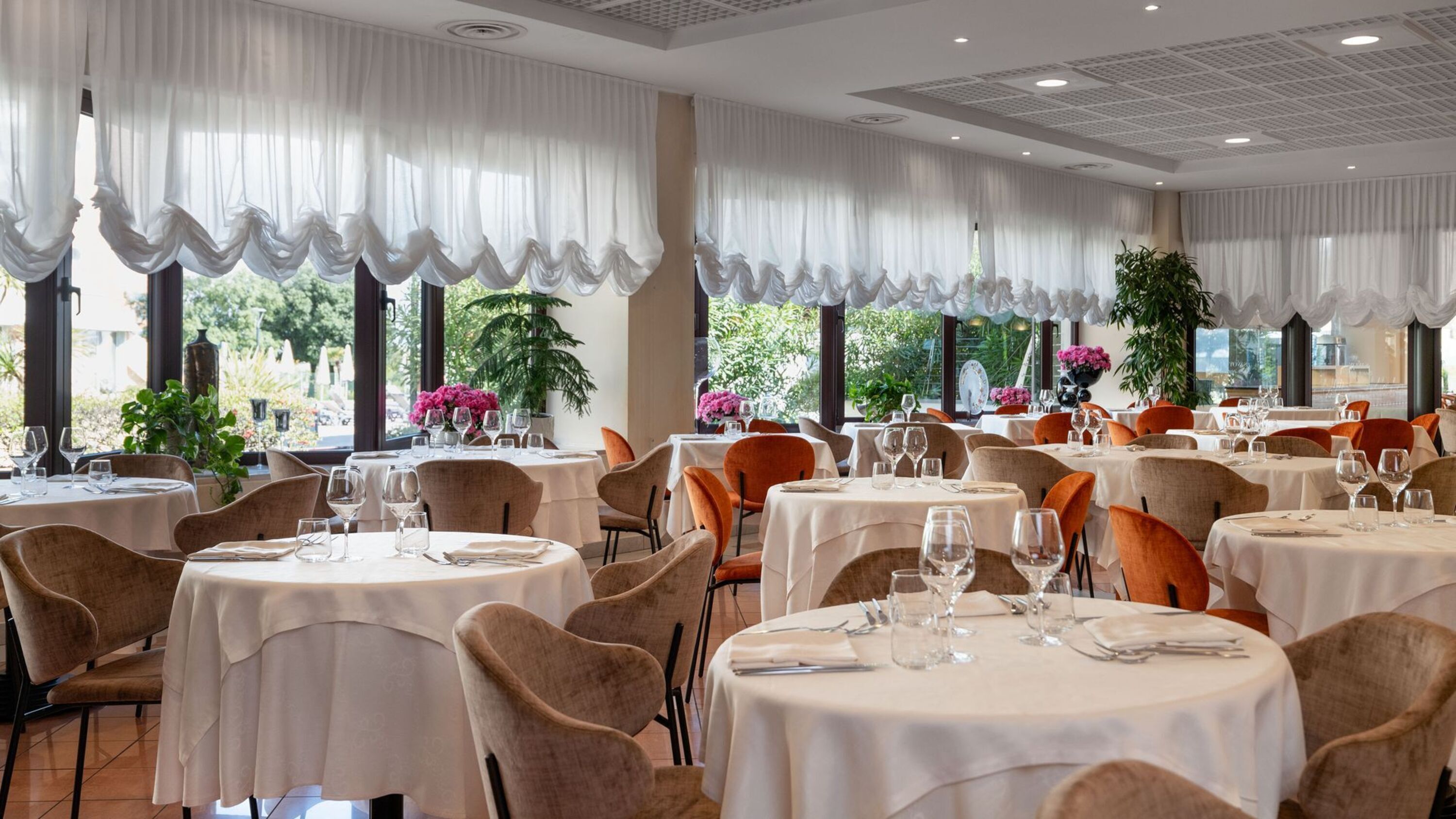 Un restaurant avec des tables rondes, des chaises et de grandes fenêtres ornées de rideaux.