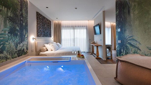 A hotel room with a large bed, a small sitting area, a TV, and a large wall mural. - Romantic suite with hydromassage tub (Bibione)