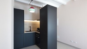 Une cuisine compacte avec des meubles de couleur sombre, un plan de travail en bois, un évier, une cuisinière et un luminaire suspendu.