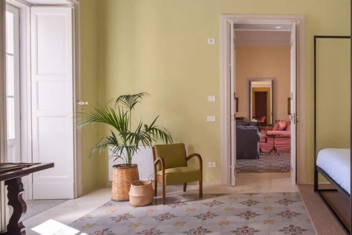 Une chambre à coucher avec un lit à baldaquin, une chaise, une plante en pot et une porte donnant sur une autre pièce.