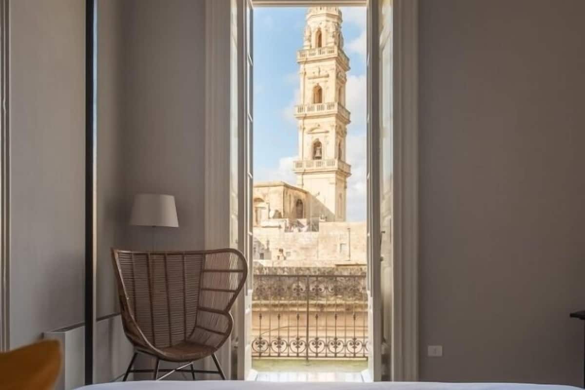 Une chambre d’hôtel avec un lit, une chaise et une vue sur une tour, visible à travers une porte ouverte.