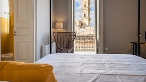 A hotel room with a bed, a chair, and a view of a tower through an open door. - PALAZZO GARZIA - Dimora Storica (Maglie)