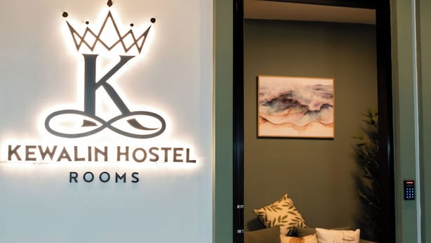 A hotel sign with a crown logo and the name "KEWALIN HOSTEL ROOMS".