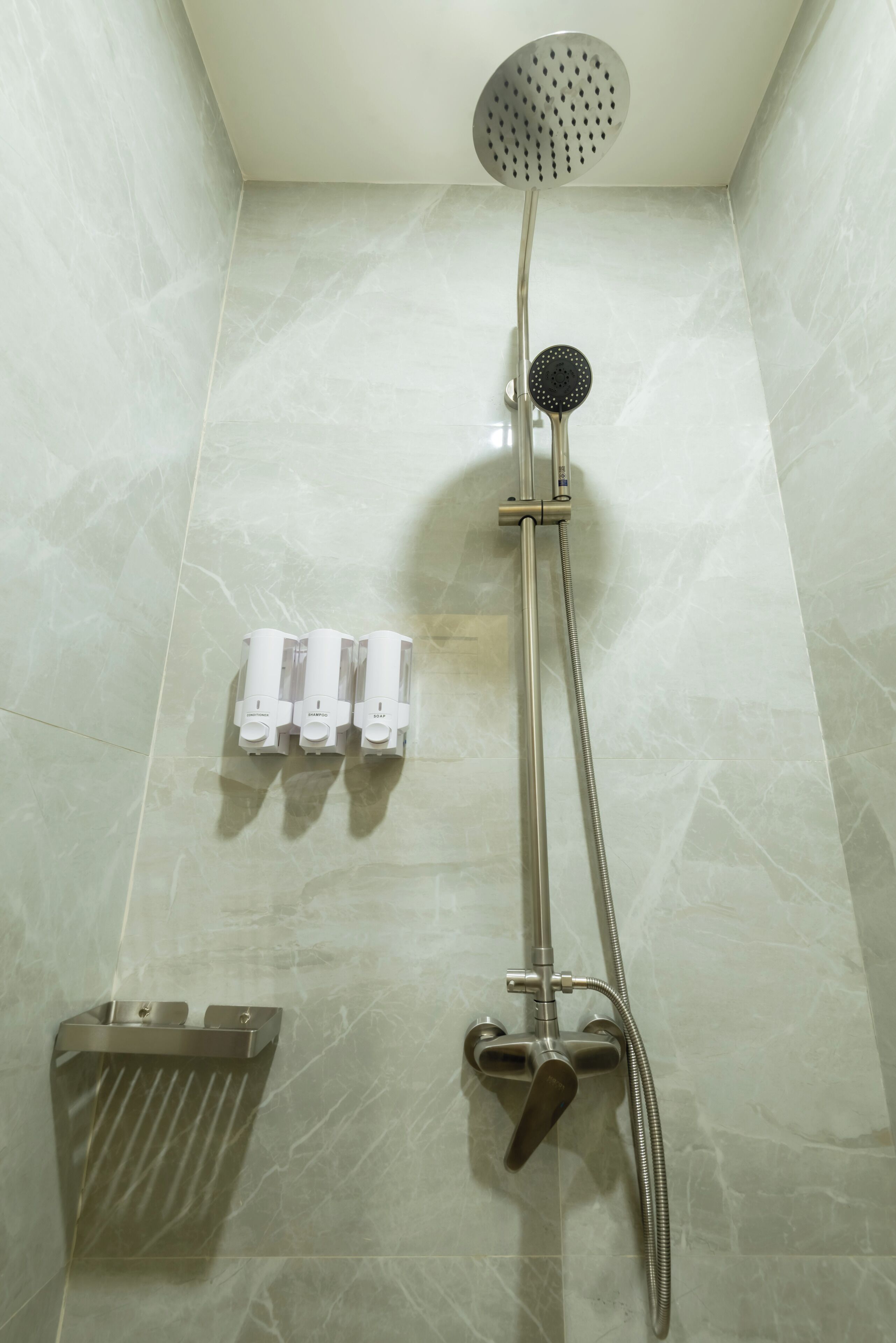 A shower with a handheld showerhead, a handheld shower attachment, and a wall-mounted faucet.