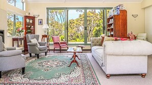 A spacious living room with a large window, a green patterned rug, and a white sofa. - Annabells Bed and Breakfast (Whitianga)