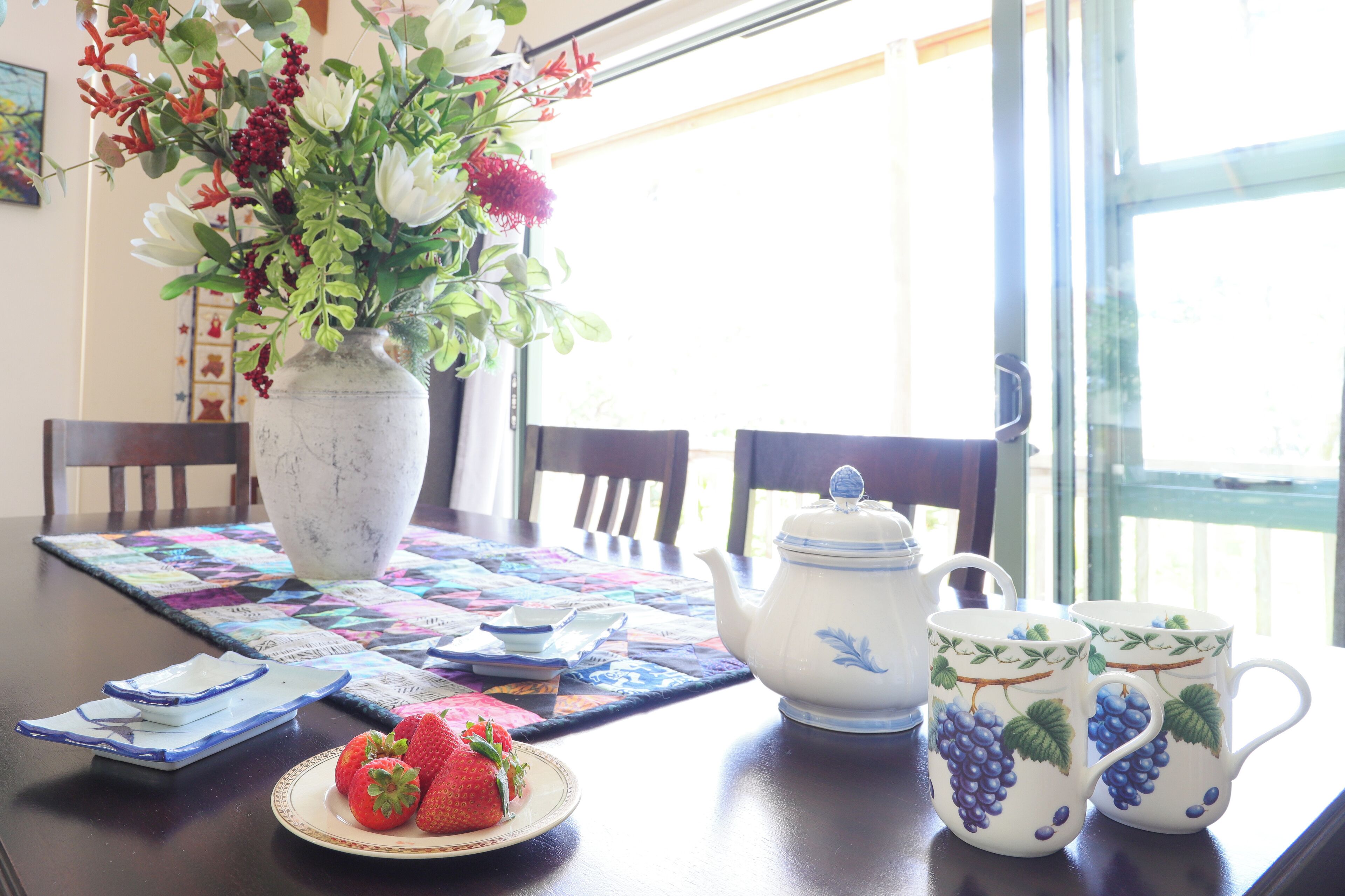 A dining table with a vase of flowers, a teapot, and two cups with a grape design.