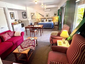 Una habitación acogedora con un sofá rojo, sillones a rayas, una mesa de madera, una cama con ropa de cama azul y una mesa de comedor.
