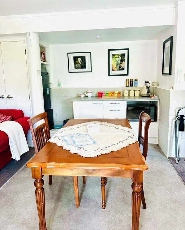 Un coin repas avec une table et des chaises en bois, une cuisine à l’arrière-plan et une porte donnant sur une autre pièce.