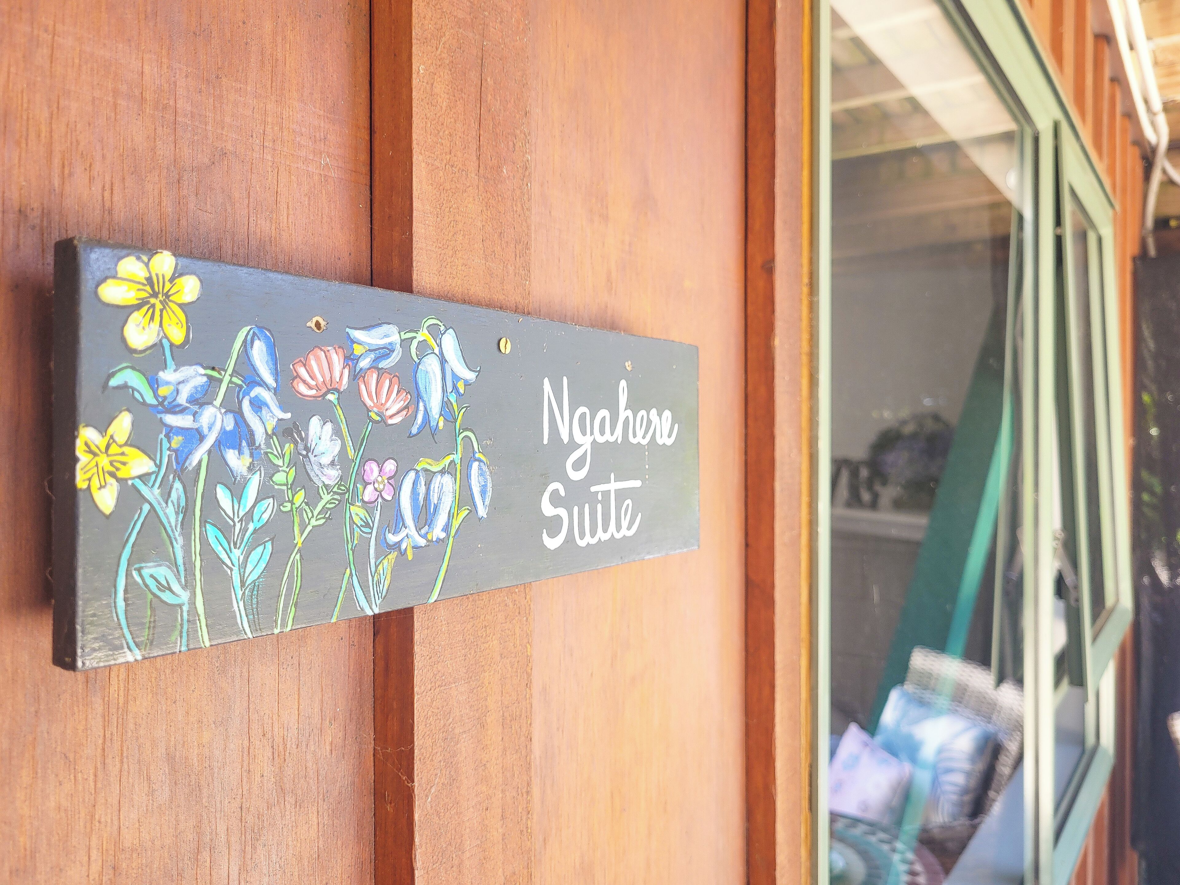 A sign with floral artwork and the text "Ngahere Suite" on a wooden wall.