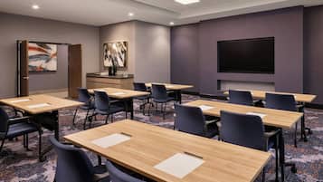 A conference room with multiple tables and chairs, a projector screen, and artwork on the walls.