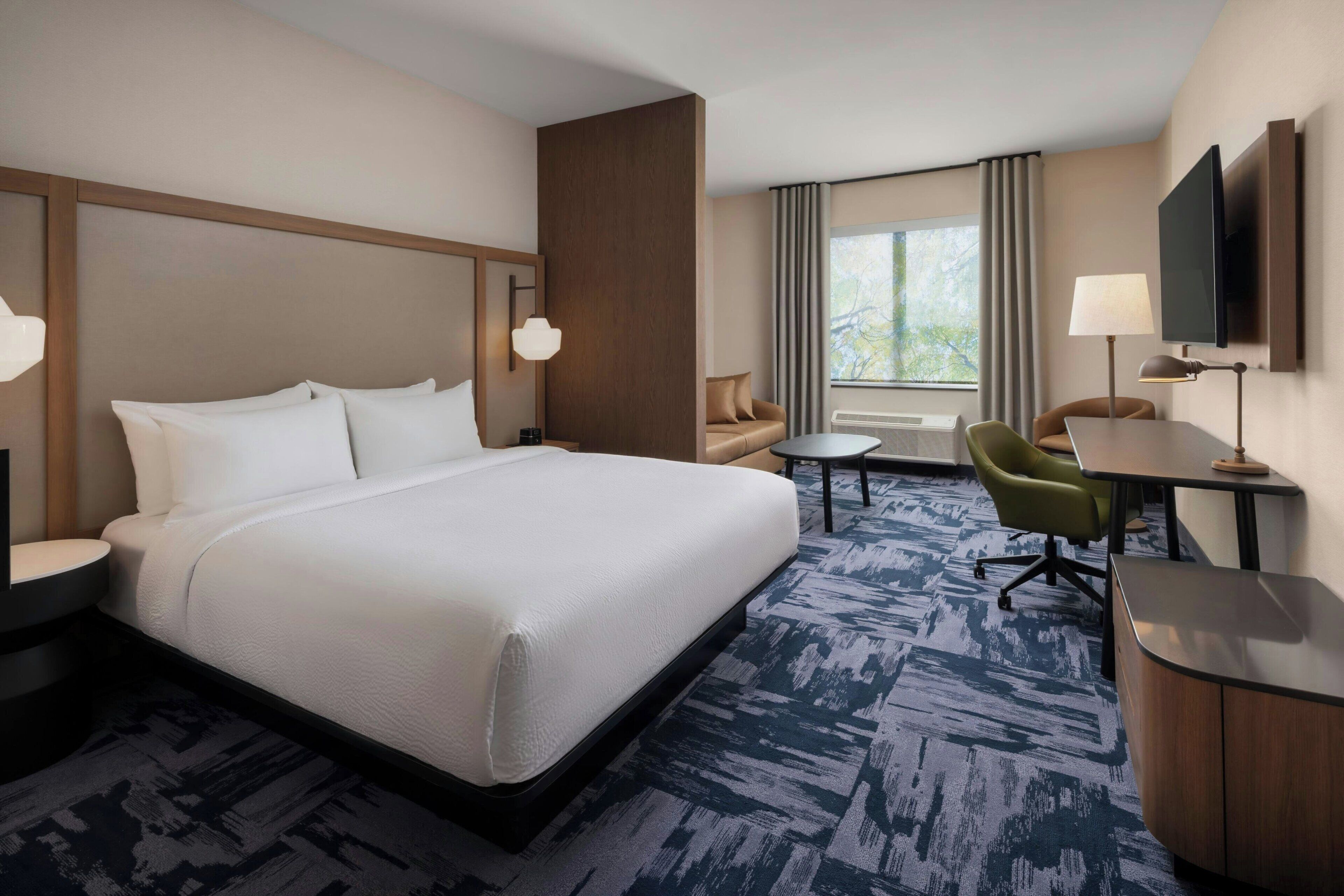 A hotel room with a large bed, a desk, a chair, a sofa, and a television.