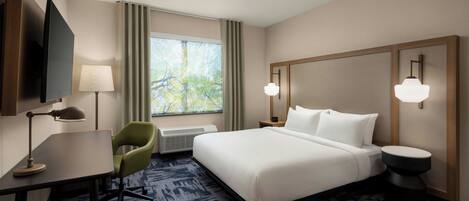 Habitación de hotel con cama, escritorio con lámpara, silla, televisor y ventana con cortinas.