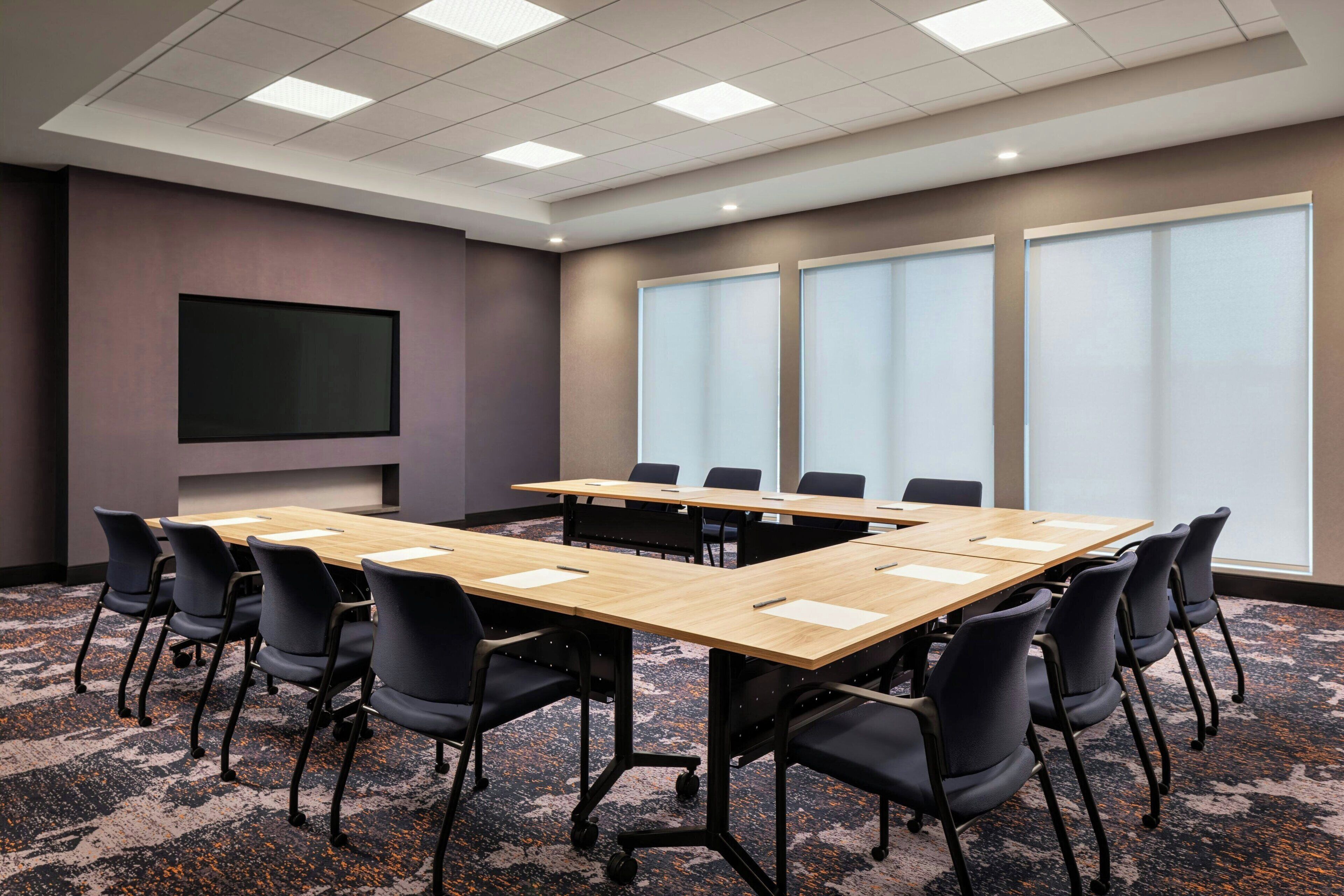 A conference room with a large table, chairs, a flat-screen TV, and large windows.