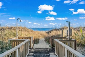 A wooden boardwalk leading to a beach with a clear sky and clouds.