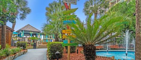 Colorful directional signs lead the way through swaying palms in this tropical pool area.