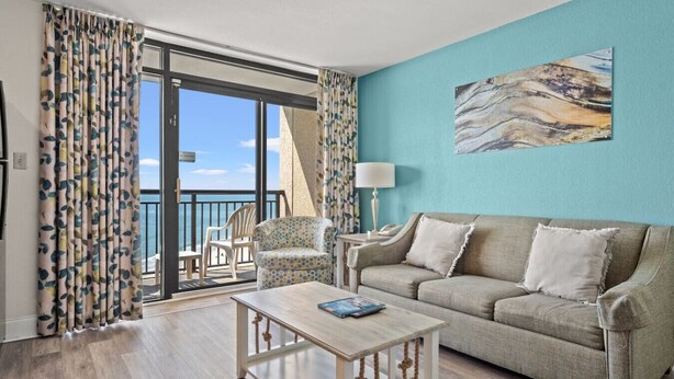 A living room with a sofa, a coffee table, and a chair. There is a balcony with a view of the sea. - Panoramic Ocean View, Lazy River (North Myrtle Beach)