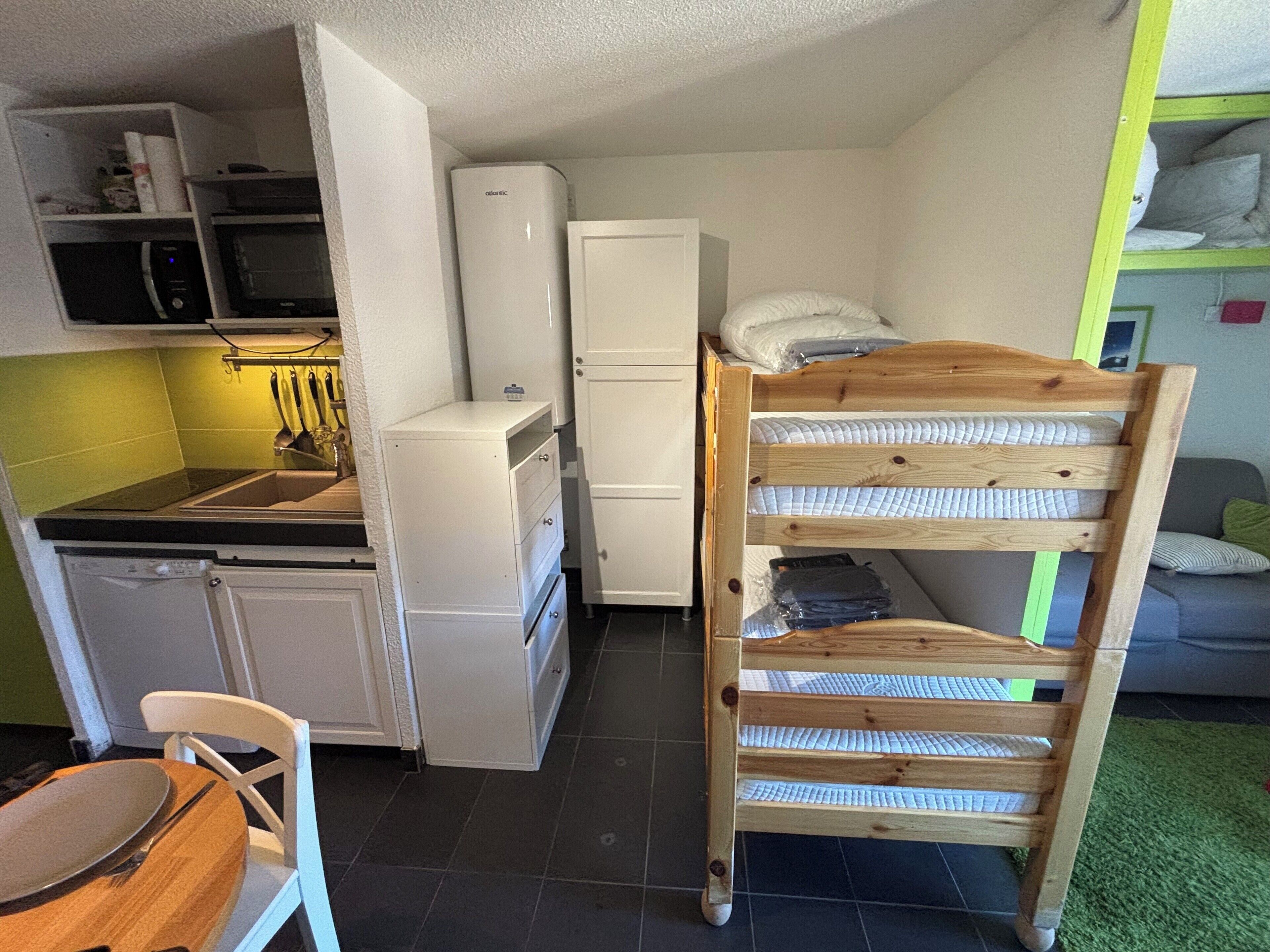 Cocina compacta con microondas, refrigerador y una litera de madera.