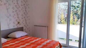 Une chambre à coucher avec un lit, un radiateur et une vue sur l’extérieur, accessible par une porte-fenêtre coulissante.