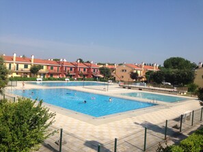 Una piscina con múltiples carriles, rodeada por una valla, junto a una hilera de edificios residenciales.