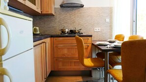 A compact kitchen with wooden cabinets, a gas stove, and a dining area with yellow chairs.