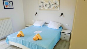 A neatly made bed with a blue bedspread, two white pillows, and two rolled towels.