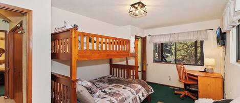 A bunk bed room with a desk and chair, a window with a view, and a door leading to another room.