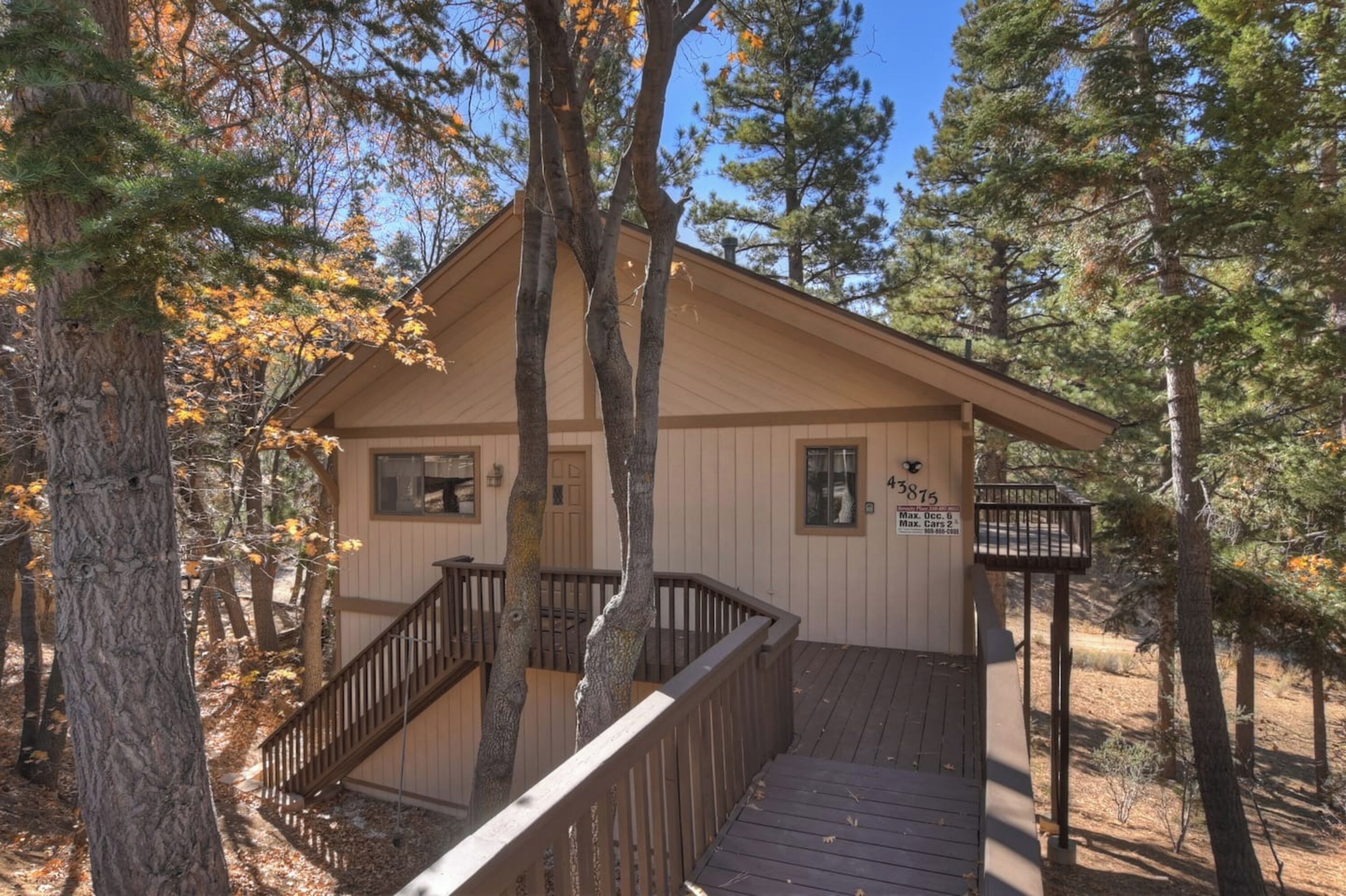A cabin with a wooden deck, a staircase, and a sign indicating a maximum occupancy of 6 people.
