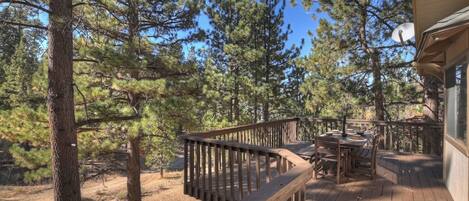 A wooden deck with a dining table and chairs, surrounded by tall pine trees.