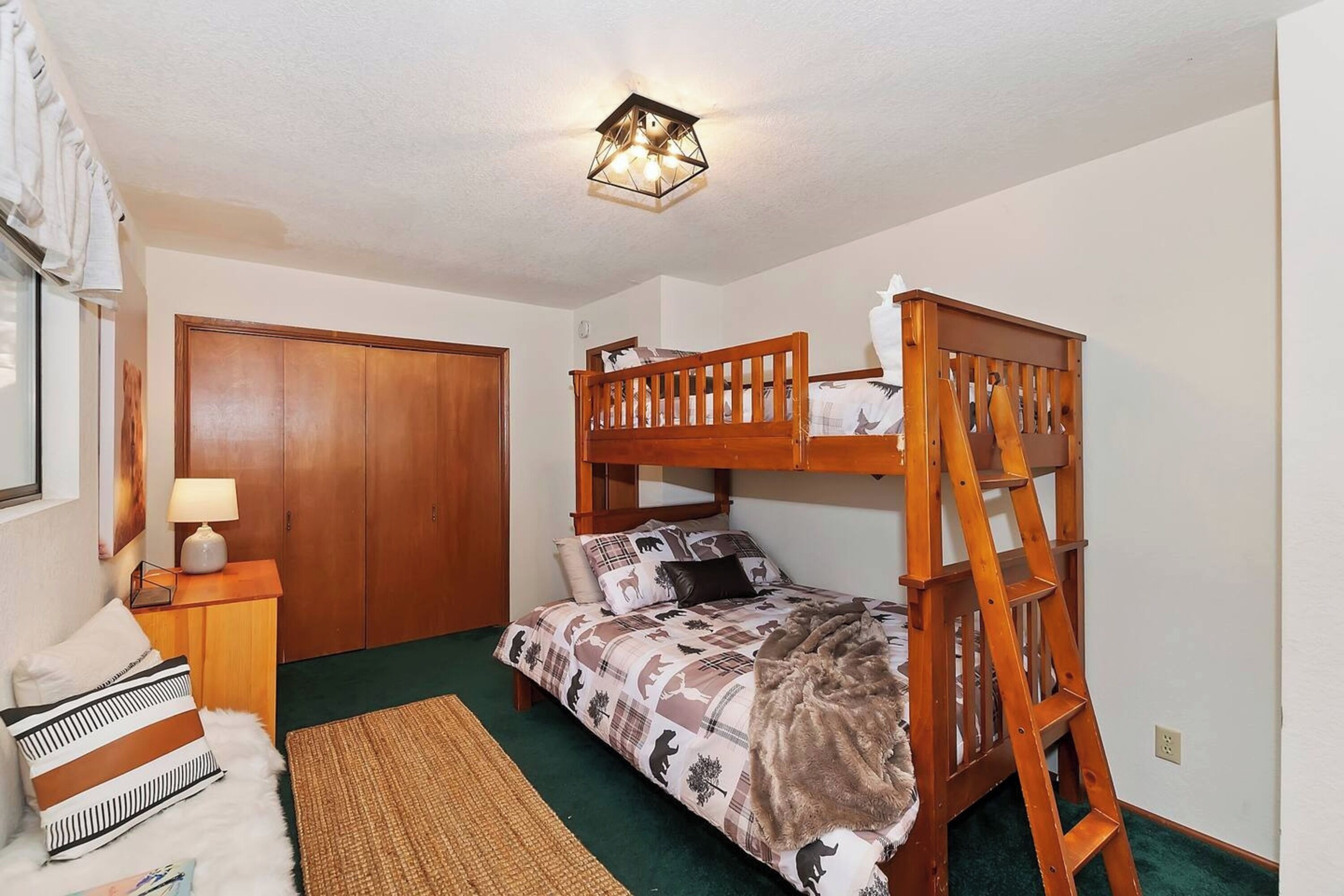 Een slaapkamer met een stapelbed, een houten kledingkast, een nachtkastje met een lamp en een groen tapijt.