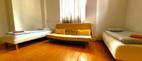 Une chambre avec deux lits simples, un canapé et un plancher en bois.