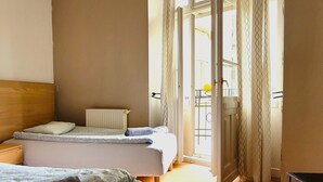 A bedroom with two beds, a wooden headboard, a radiator, and a view of the outside through a door with curtains. - Central Station Hostel (Warsaw)