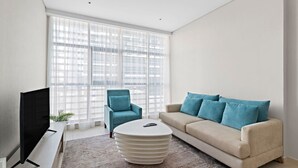 Un saló modern amb televisió de pantalla plana, un butac armchair blau, un sofà beix amb coixins blaus i una taula de cafè blanca.