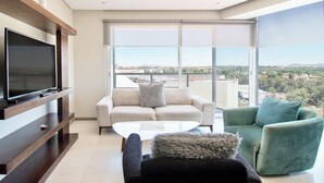 A modern living room with a flat-screen TV, a sofa, a coffee table, and a view of a cityscape through large windows. - Apartment in plaza pabellon zone andares (Guadalajara)