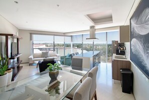 A modern living room with a glass coffee table, sofas, and a large window offering a city view.