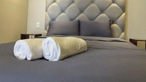 A neatly made bed with a tufted headboard, two pillows, and two rolled towels. - Apartment in plaza pabellon zone andares (Guadalajara)