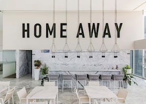 A modern interior with a 'HOME AWAY' sign, marble flooring, and a dining area with white furniture.