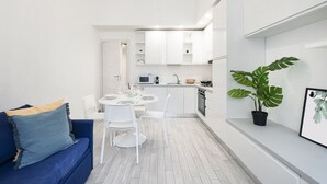 A modern kitchen with white cabinets, a dining table with chairs, and a blue sofa with cushions.