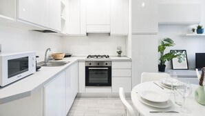 A modern kitchen with white cabinetry, a built-in oven, a microwave, and a dining area with a table set for two.