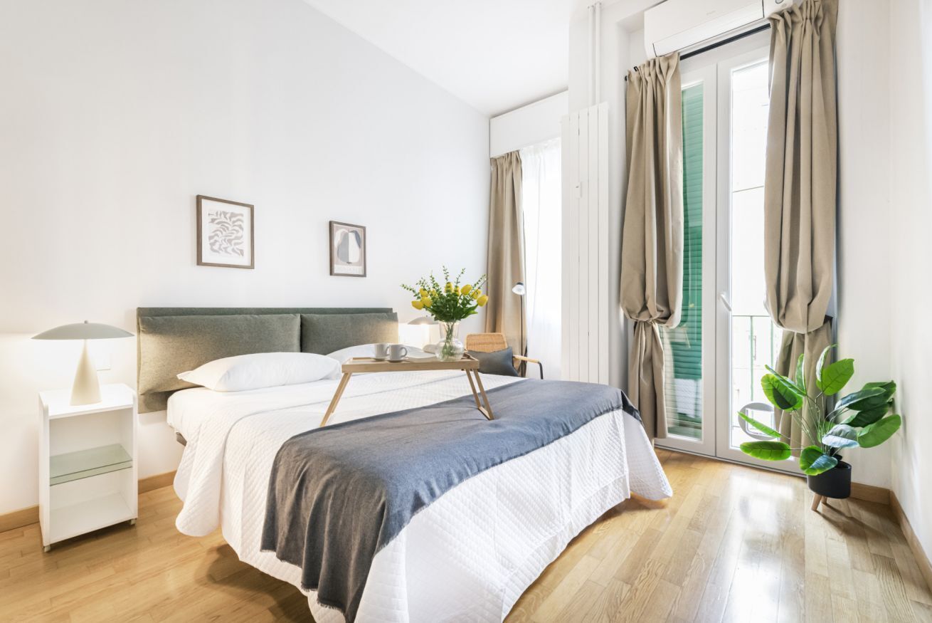 Une chambre à coucher avec un lit, une table de chevet, une lampe et une fenêtre avec des rideaux.