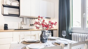 Una cocina moderna con armarios blancos, una mesa de comedor dispuesta con platos y vasos, y un jarrón con flores rojas.