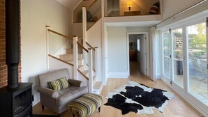 A spacious living area with a fireplace, a sofa, a patterned ottoman, a cowhide rug, and a staircase leading to a loft. - Charming countryside retreat (Cross in Hand)