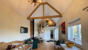 A spacious loft-style living area with a high ceiling, wooden beams, a dining table, and a large window providing natural light. - Charming countryside retreat (Cross in Hand)