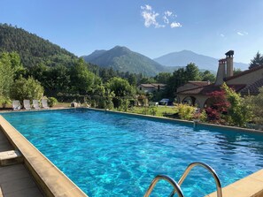A swimming pool with clear blue water, surrounded by lush greenery and a mountainous backdrop.