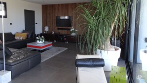 A modern living room with a sofa, coffee table, and a large potted plant. - L'Ecrin contemporain (Nages-et-Solorgues)