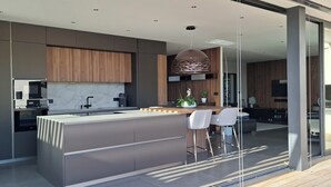 A modern kitchen with a central island, bar stools, and a large window. - L'Ecrin contemporain (Nages-et-Solorgues)