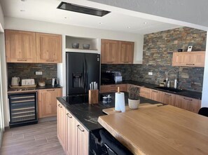 A modern kitchen with wooden cabinets, a black refrigerator, a stone backsplash, and a wooden island with a sink. - Magnificent villa with panoramic sea view (Biot)