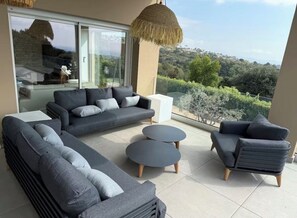 A modern outdoor seating area with a sofa, armchairs, and round tables, overlooking a scenic landscape. - Magnificent villa with panoramic sea view (Biot)