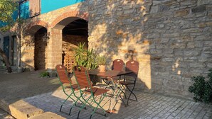 Une terrasse avec un mur en pierre, une table en bois et des chaises en métal vert.